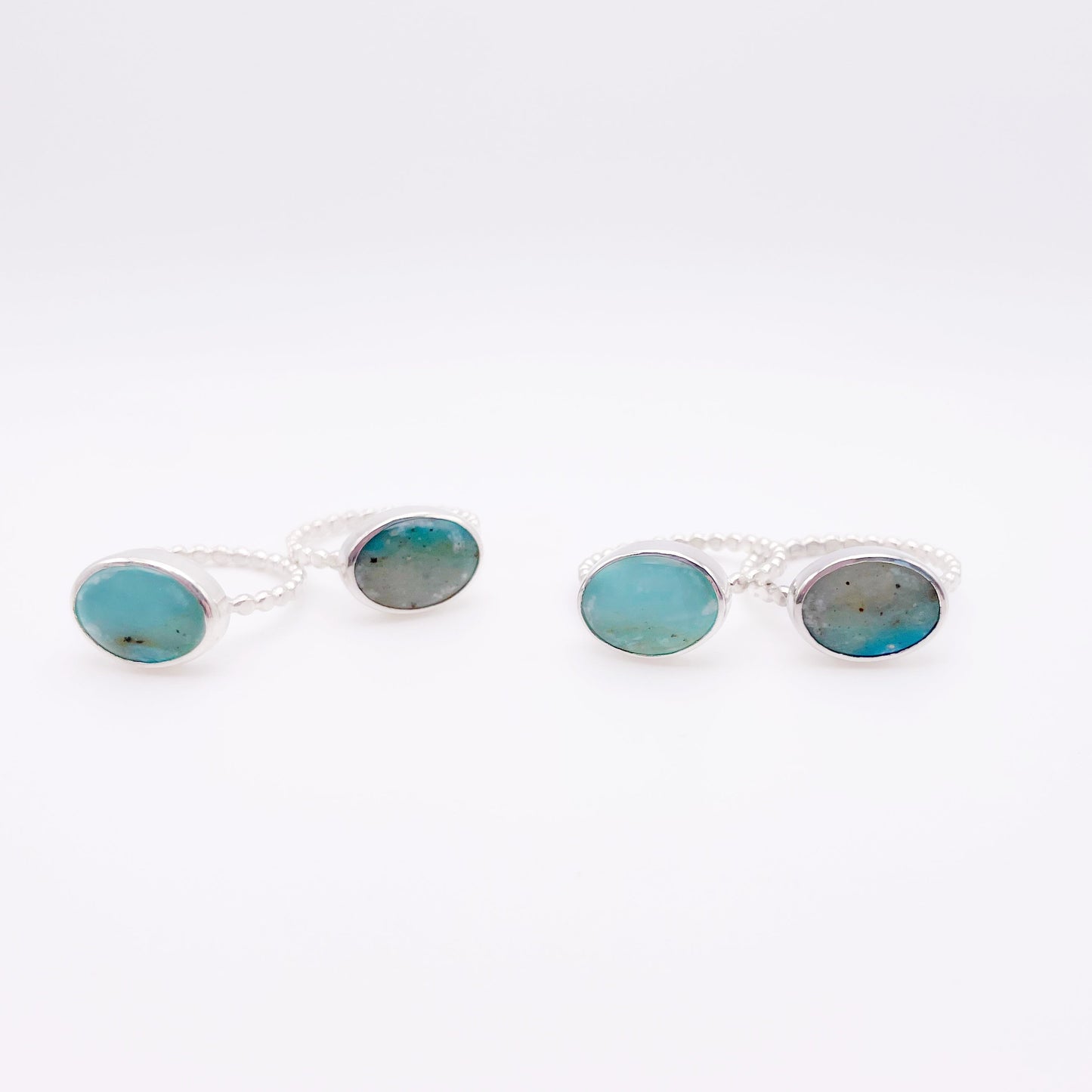Set of four silver rings with a beaded band featuring an oval-shaped gemstone with a gradient of gray and blue hues, set against a white background.