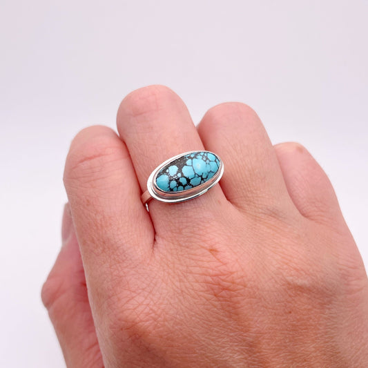 Hand wearing a silver ring with a horizontal turquoise stone on a white background