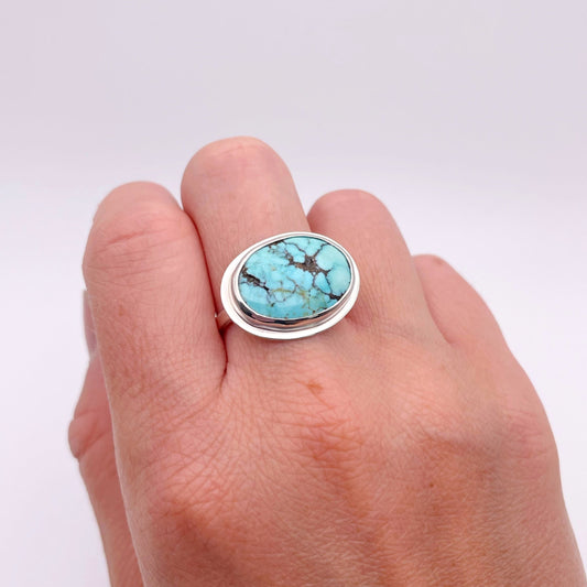 Hand wearing a ring with a turquoise stone on a white background