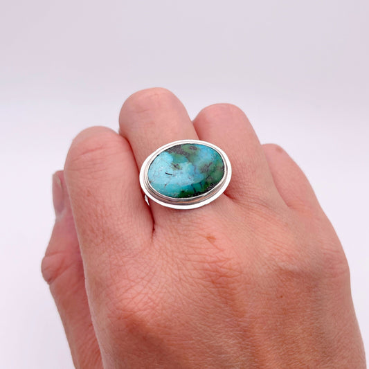 Hand wearing a ring with a turquoise stone on a white background