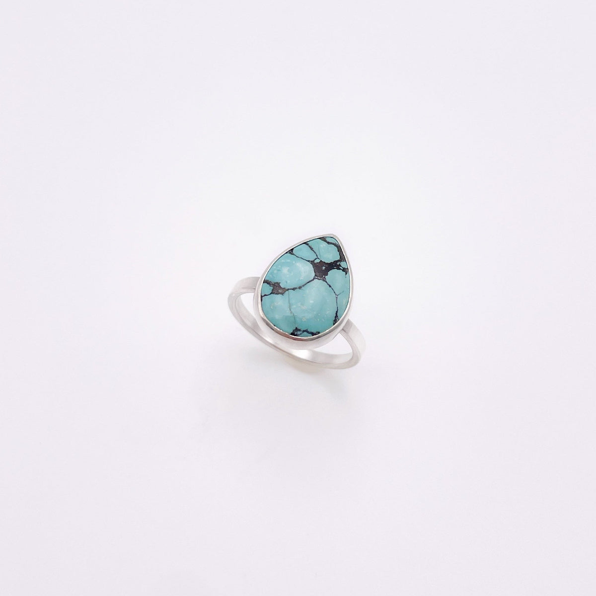 A silver ring featuring a teardrop-shaped turquoise stone with dark matrix veining, set against a plain white background.
