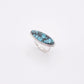 A silver ring featuring an oval turquoise stone with dark matrix, displayed on a clean white background.