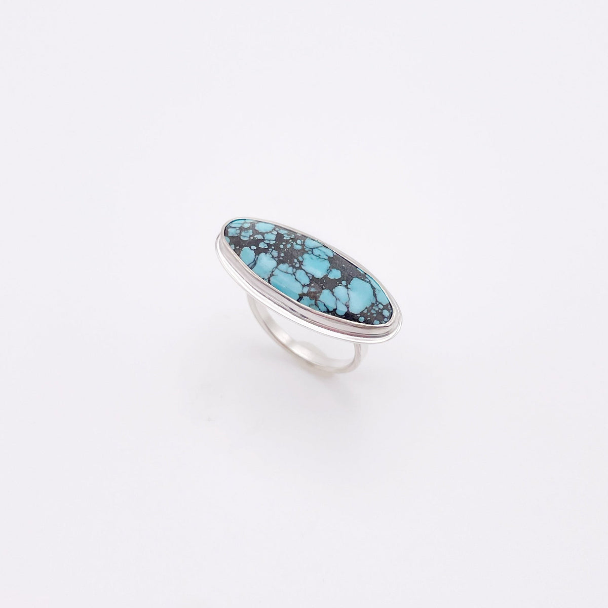 A silver ring featuring an oval turquoise stone with dark matrix, displayed on a clean white background.