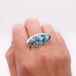 A silver ring featuring an oval turquoise stone with dark matrix, worn on a person's hand against a plain white background.