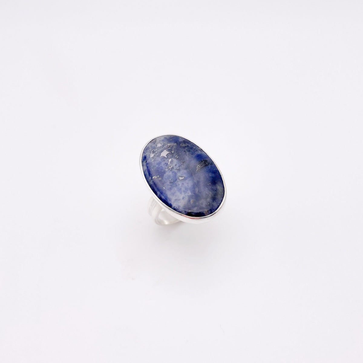 A silver ring featuring an oval-shaped cabochon sodalite gemstone with natural blue and white cloudy patterns, set against a plain white background.