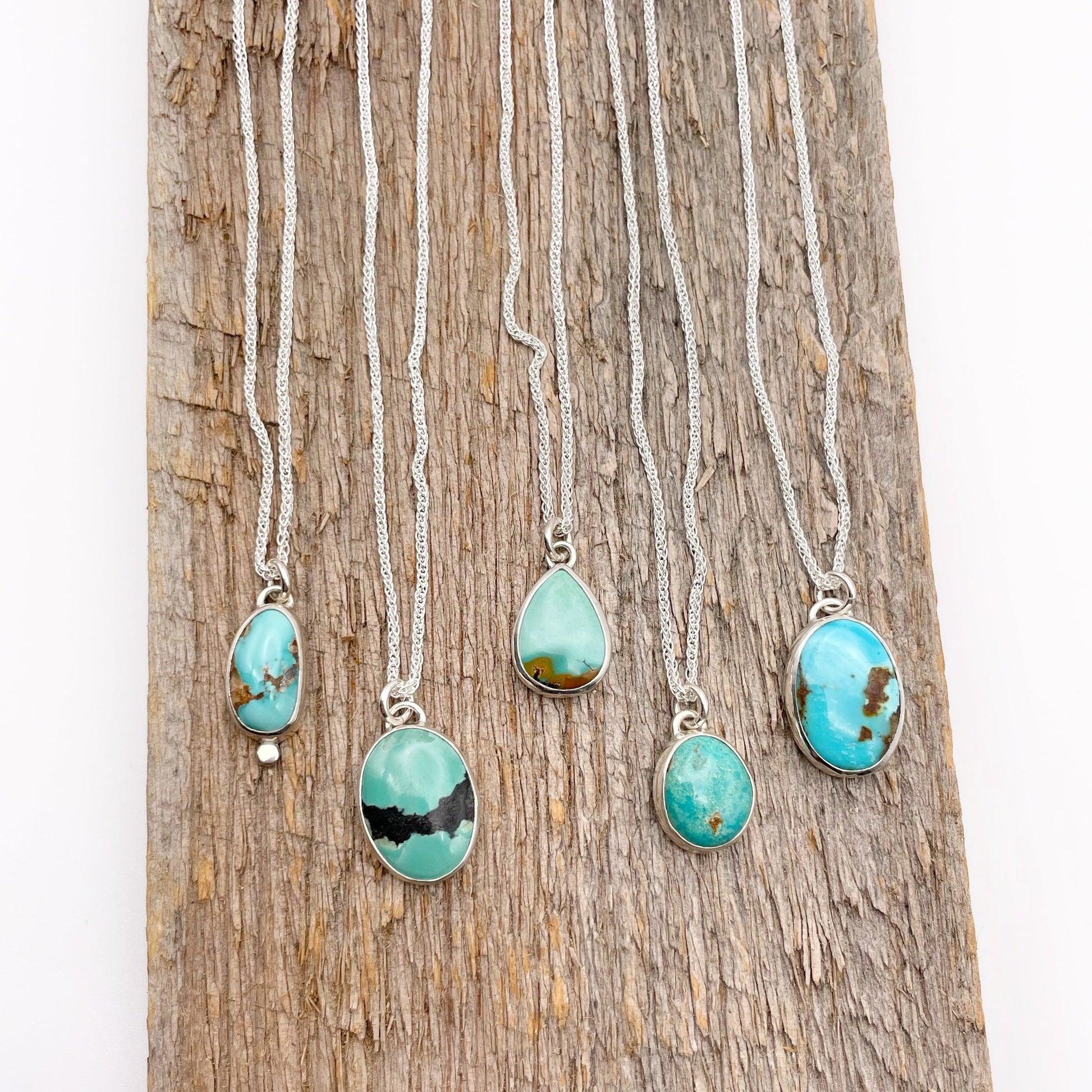 Five turquoise and sterling silver necklaces laying vertically on wood. 