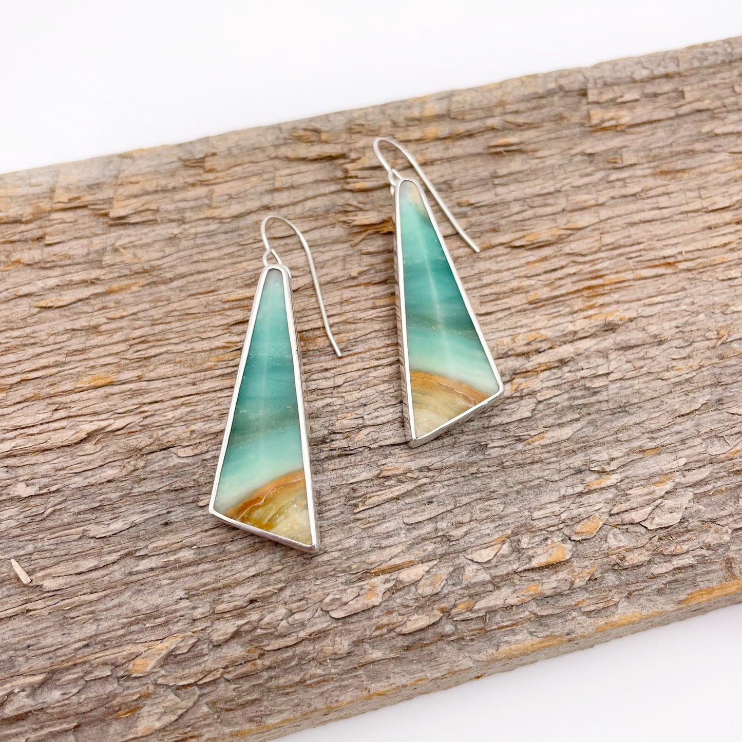 Teal and gold triangle-shaped earrings on a wooden surface