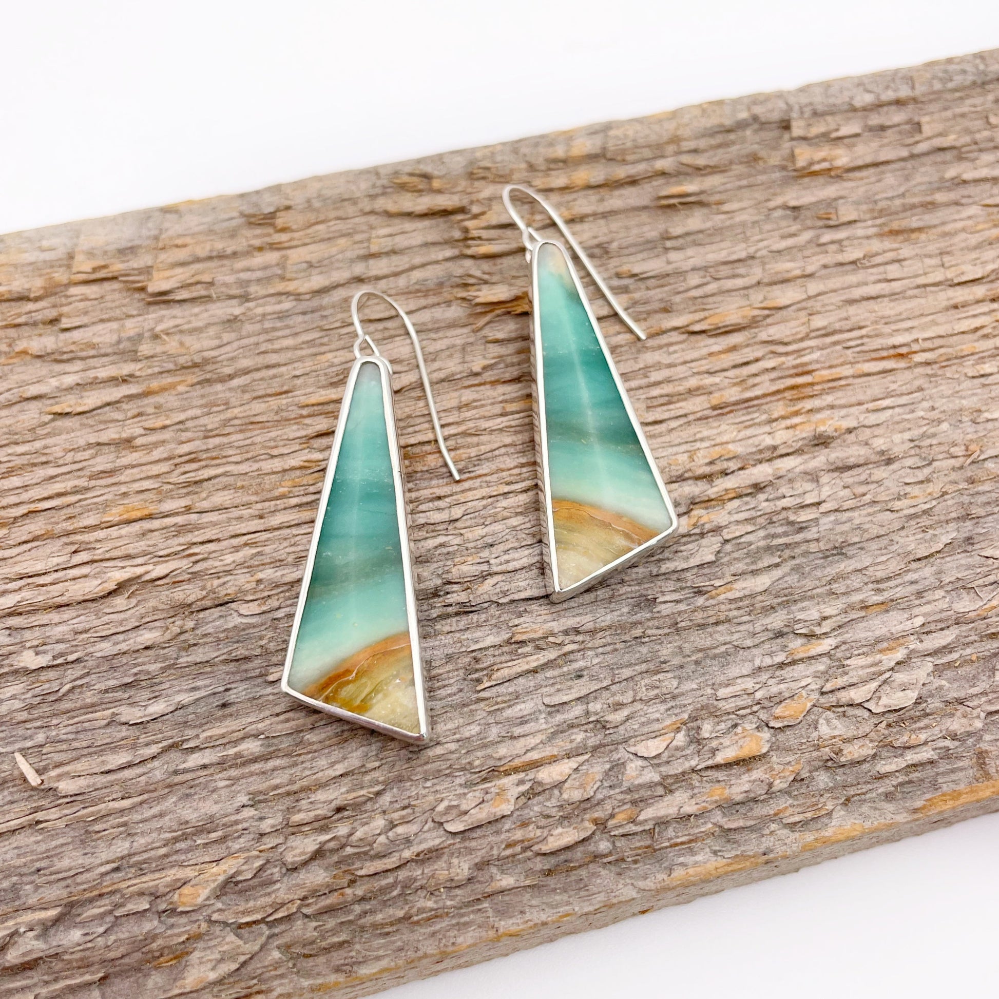 Teal and gold triangle-shaped earrings on a wooden surface