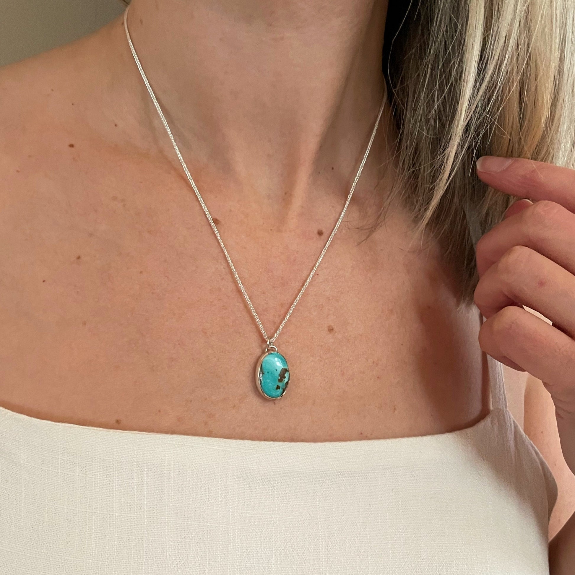 A vertical oval of blue green turquoise with a small bail on top and hanging from a delicate silver link chain on neck model